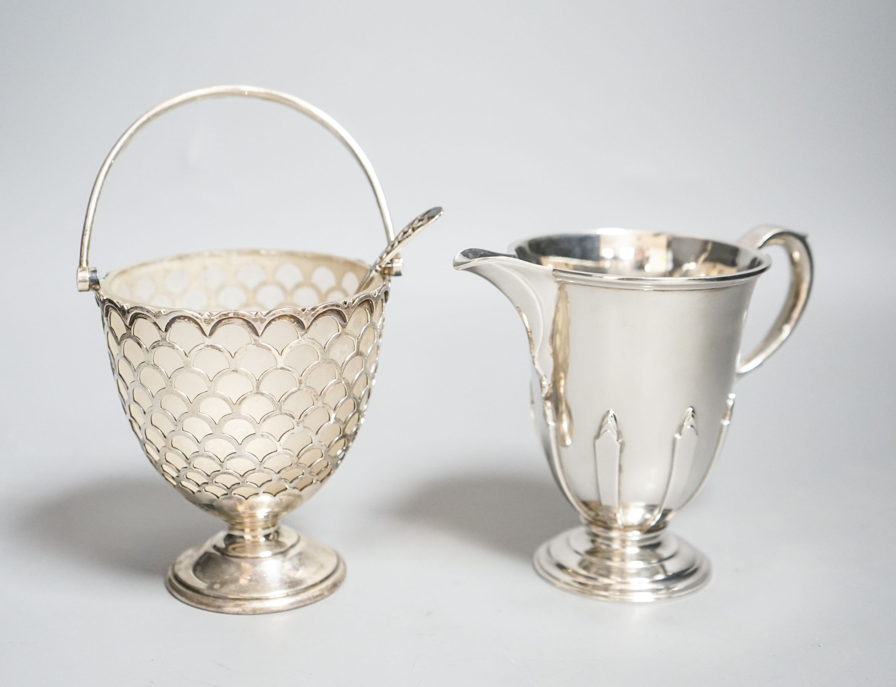 A modern silver sugar basket and sifter spoons, with glass liner by Mappin & Webb, 9.8cm and an earlier silver cream jug by William Comyns & Sons Ltd.